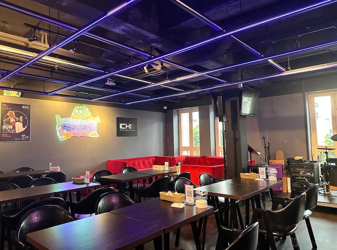 An event space in a bar with black tables and chairs, neon wall sign, red couch seating, and exposed ceiling at Ichi Singapore.