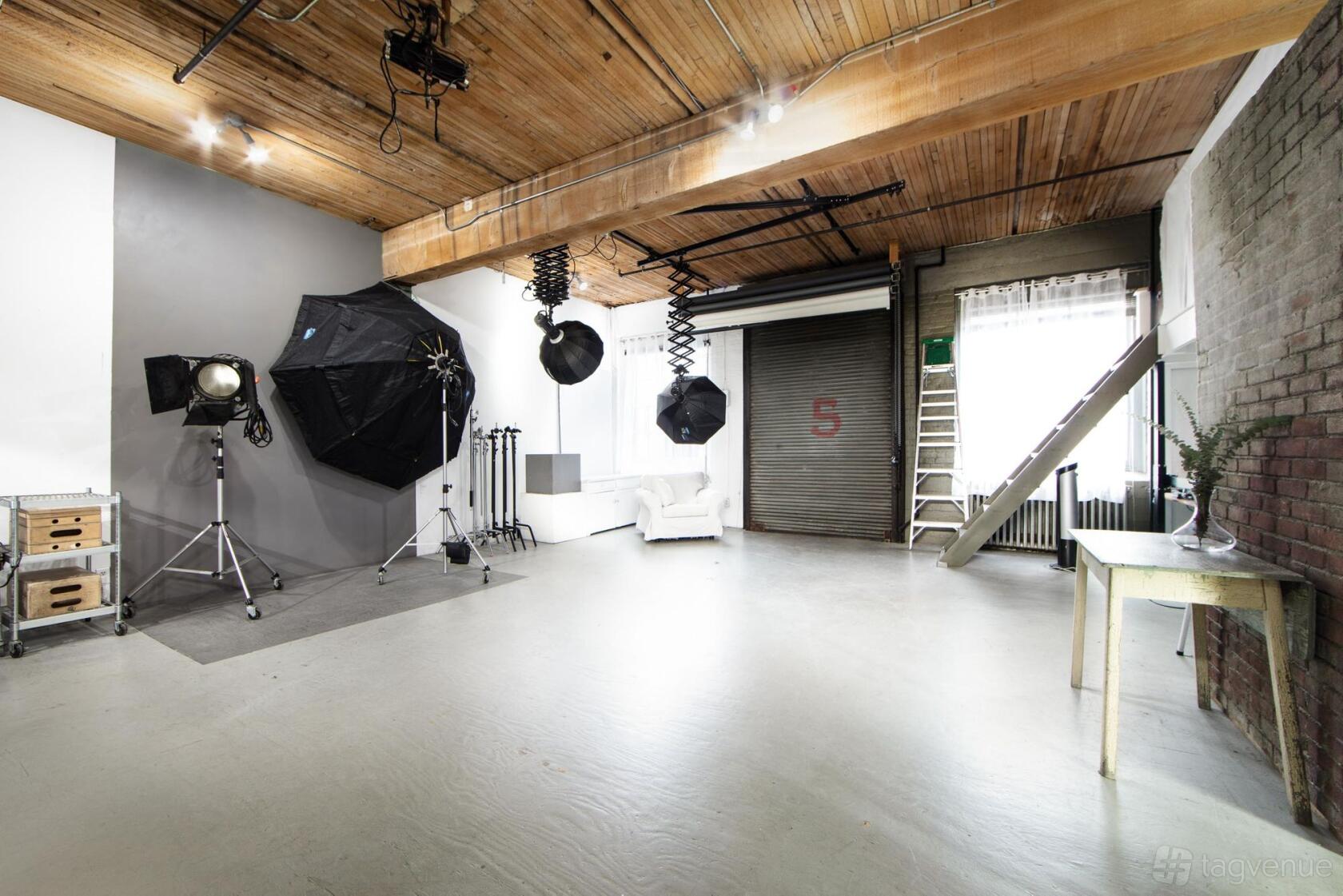 A photo studio with wood beam ceiling, studio lighting equipment, concrete floor, and a roll-up garage door at Kevin Clark Studios.