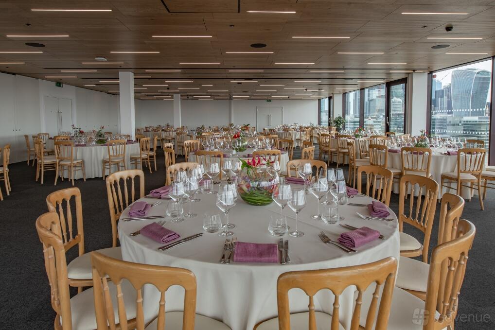 A meeting room with round tables covered in white linens, wooden chairs, and large windows at Rose Court Events.