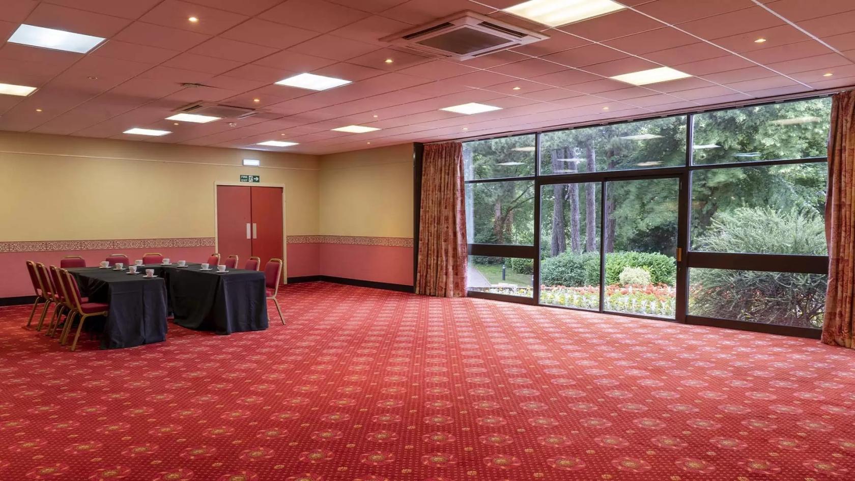 A function room with red patterned carpet, large windows overlooking gardens, and a meeting table at Sutton Coldfield Town Hall.