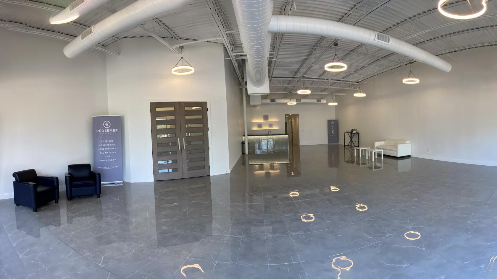A lounge with polished tile floors, white walls, and exposed ductwork at The Lightbox.