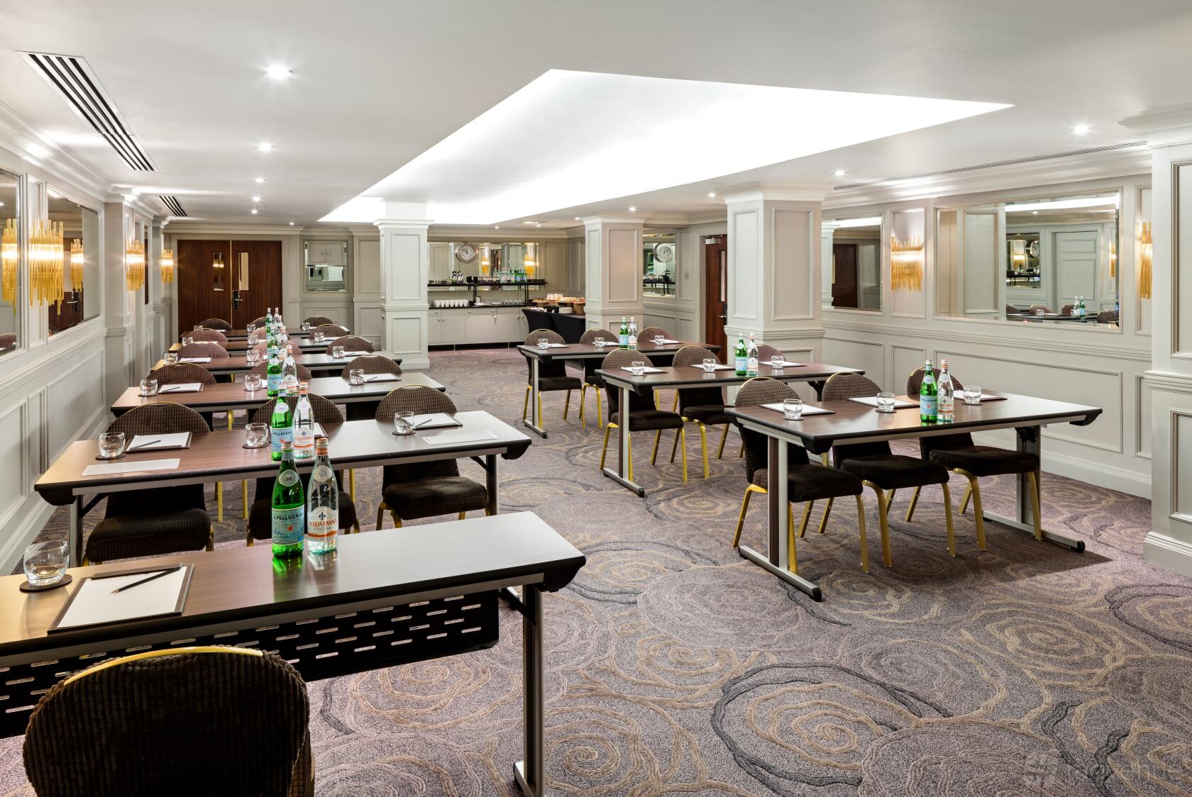 A meeting room with spaced rows of tables, bottled water, and notepads under recessed lighting at Radisson Blu Hotel, London Euston Square.