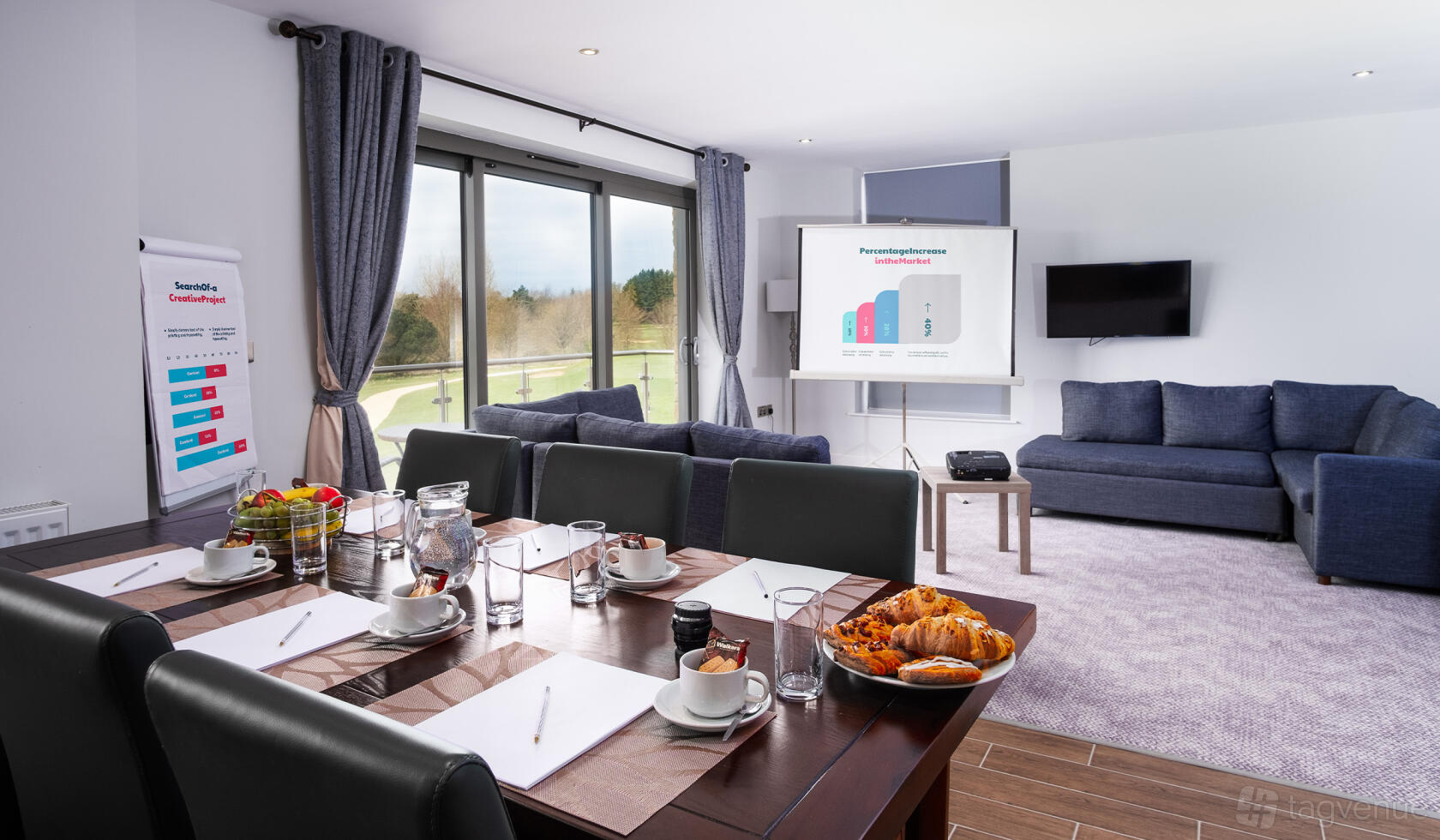 A meeting room with a large table, leather chairs, a projector screen, and floor-to-ceiling windows at Cotswolds Hotel & Spa.