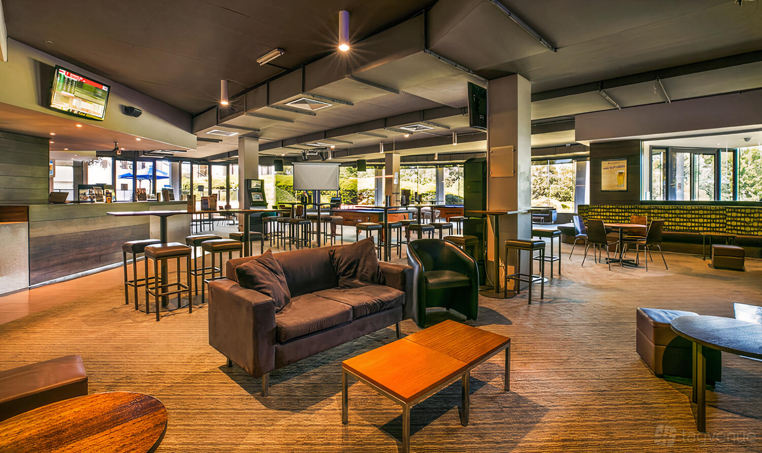 A hotel bar with cushioned sofas, high tables, bar seating, and large windows at Manningham Hotel.