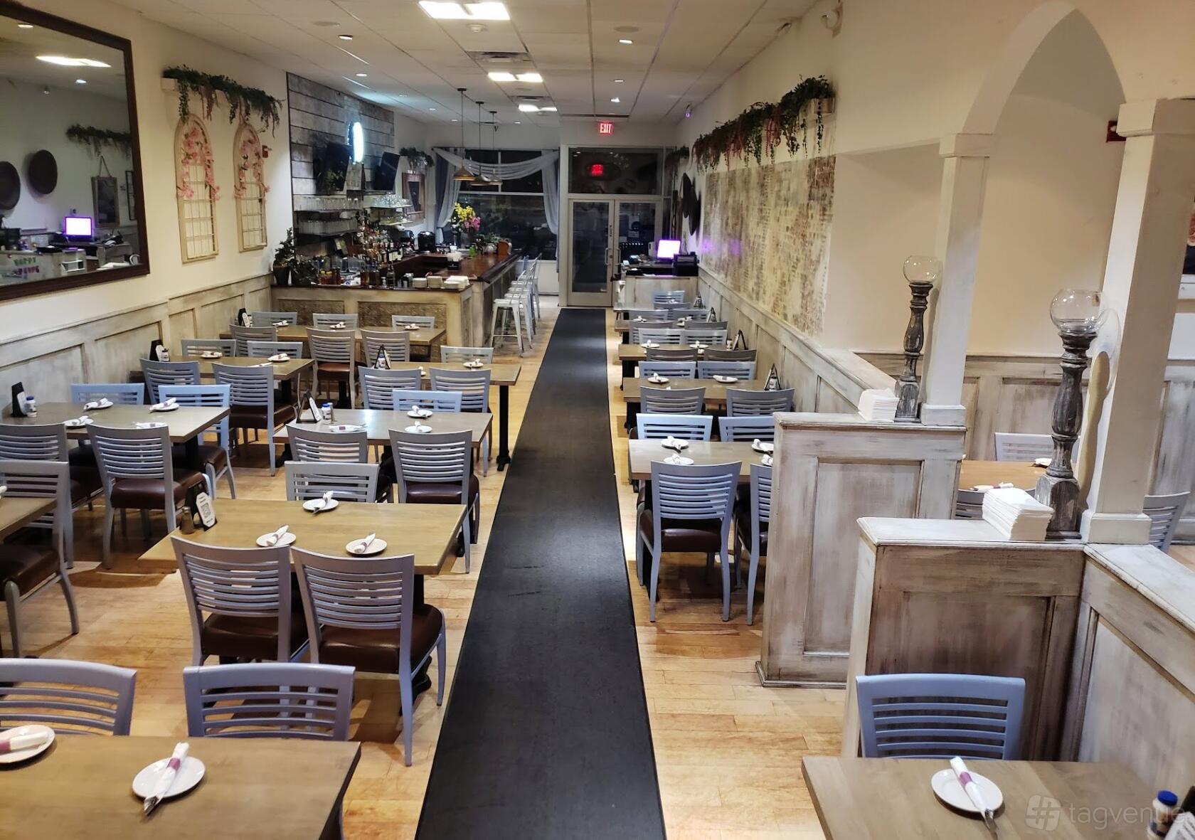 A restaurant dining room with rows of wooden tables, gray chairs, and rustic white paneling at Opa Grille.