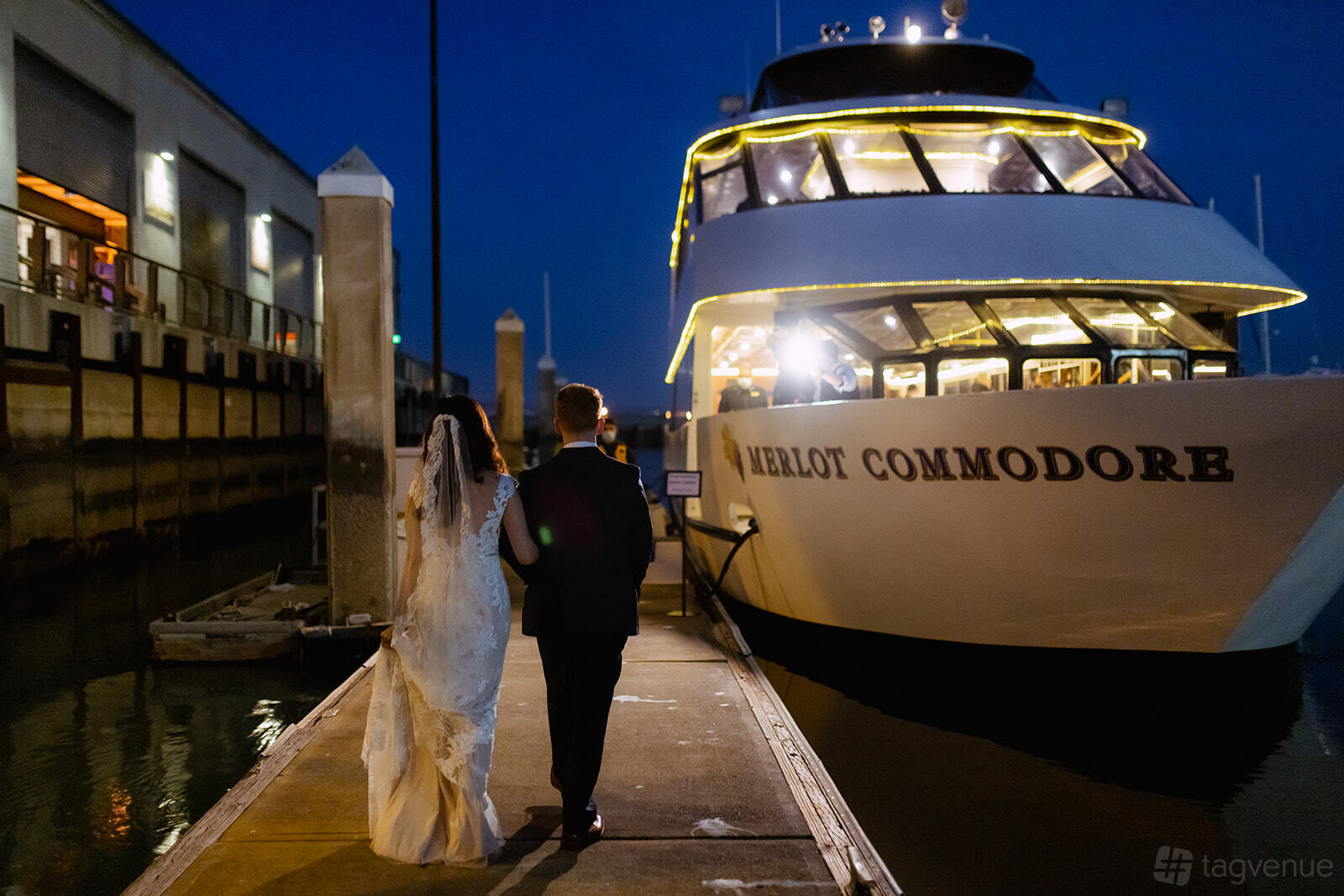 A docked yacht with illuminated railings and guests walking toward the boarding area at Merlot Yacht.