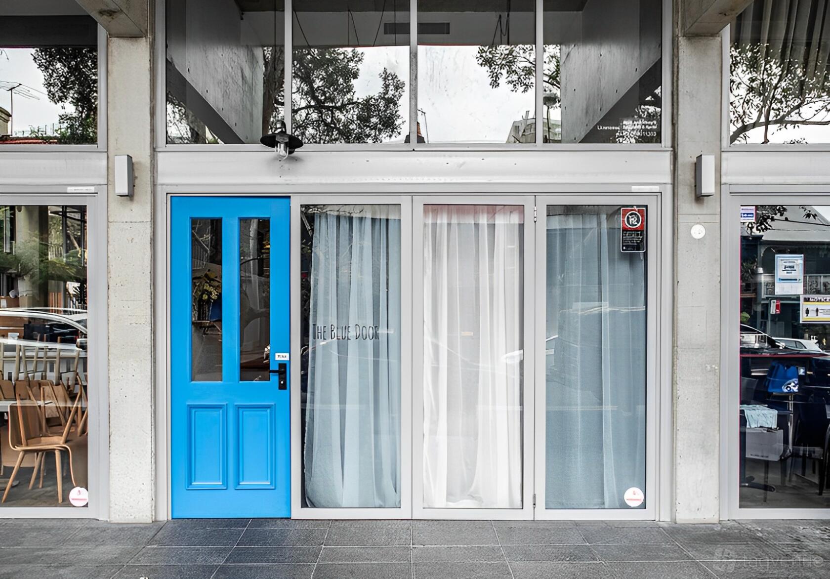 A restaurant with a bright blue entry door and floor-to-ceiling glass windows at The Blue Door.