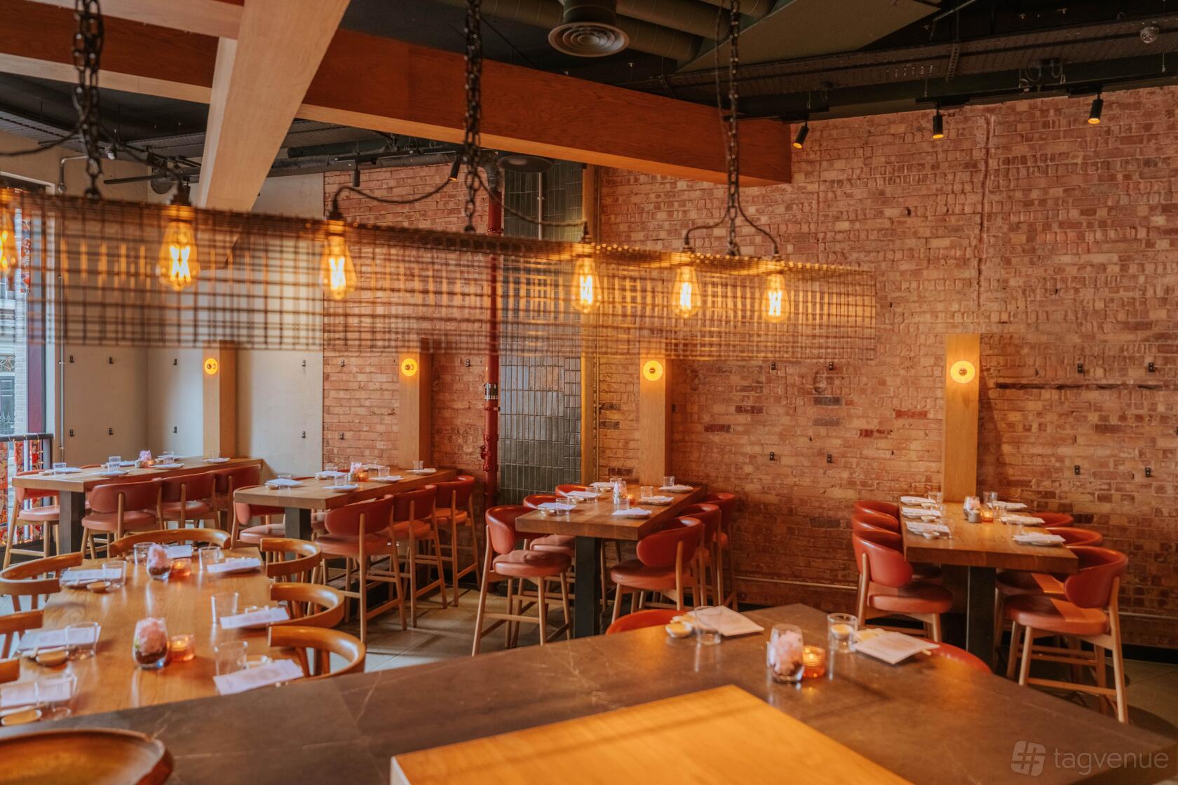 An event space in a restaurant with exposed brick walls, warm pendant lighting, and wooden tables at INKO NITO London.