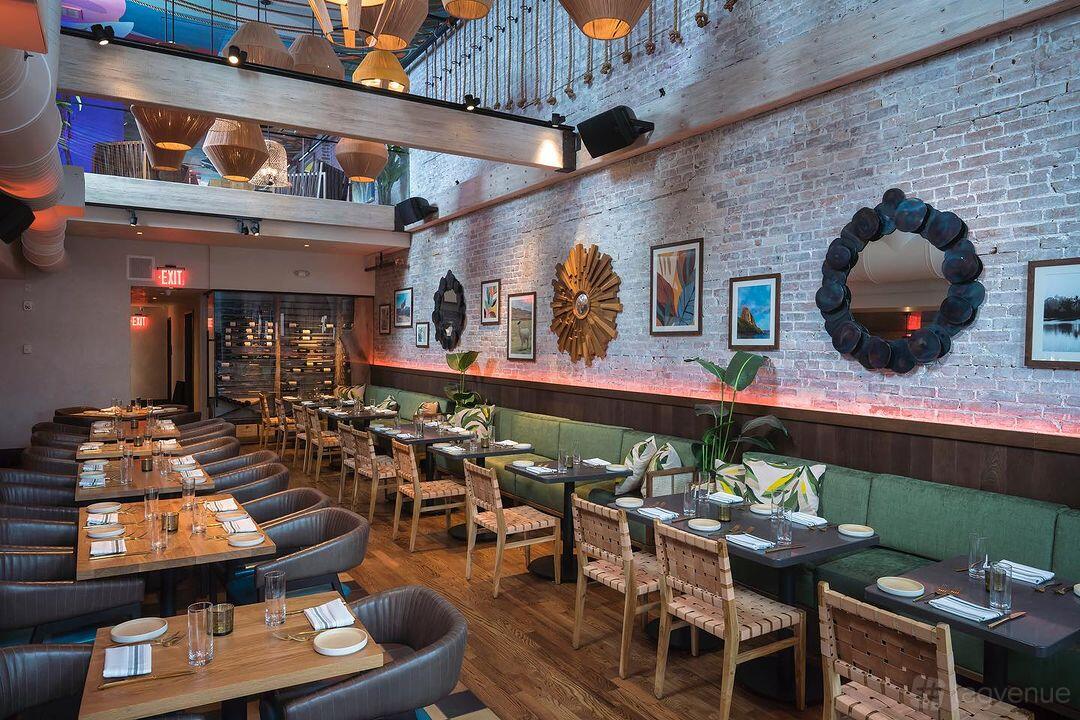 A restaurant with exposed brick walls, decorative mirrors, framed art, and wood tables with cushioned chairs at Centrada Cocina & Cocktails.