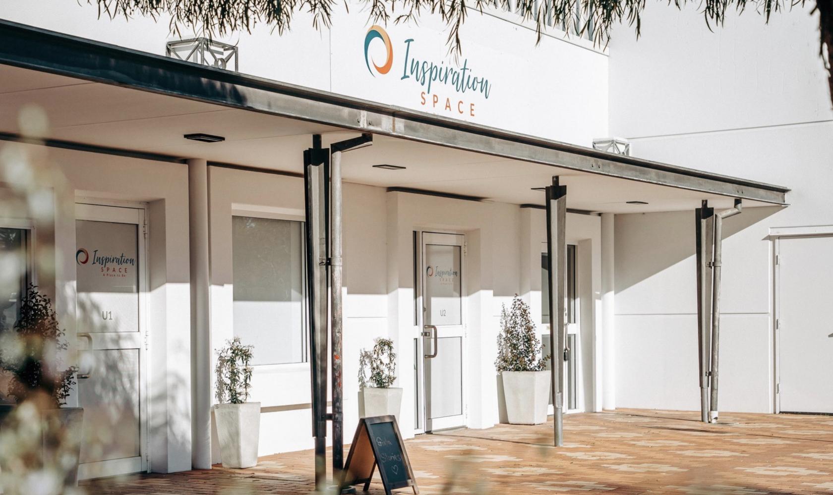 A versatile event space with a white exterior, covered walkway, and potted plants at Inspiration Space - A Place To Be.