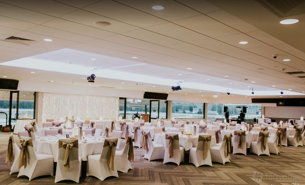 A lounge with round tables draped in white linens and gold sashes on chairs at The Entertainment Grounds.