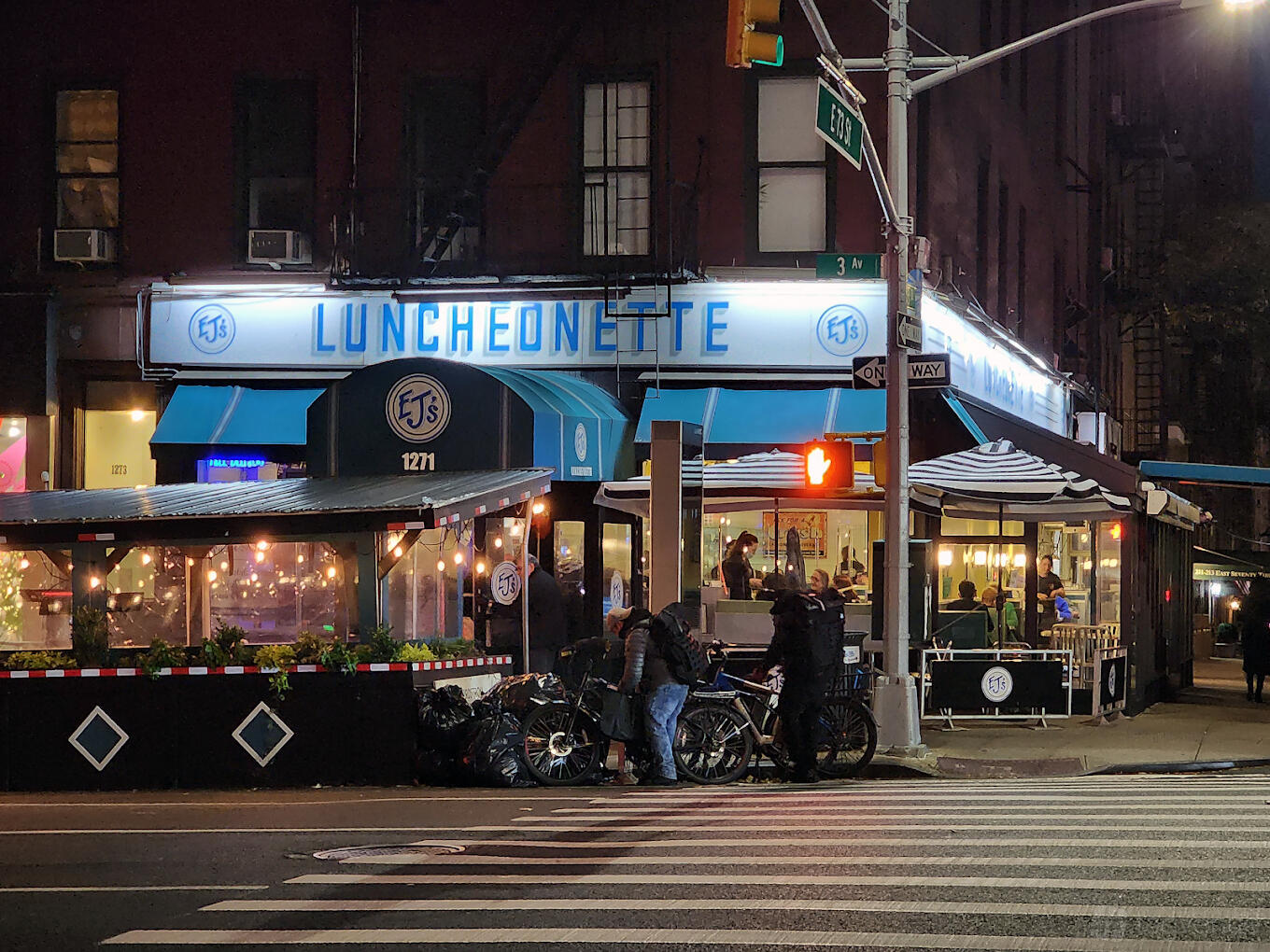 A corner restaurant with retro diner signage, striped awnings, and outdoor seating at EJ's Luncheonette.