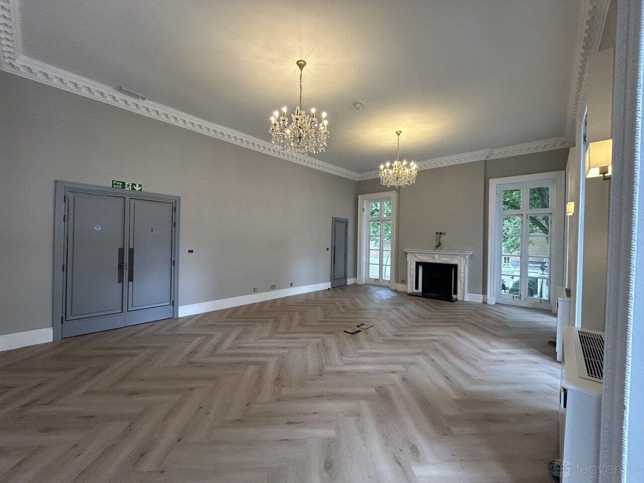 An event space with herringbone wood floors, chandeliers, and large windows at Noura Lounge Mayfair.