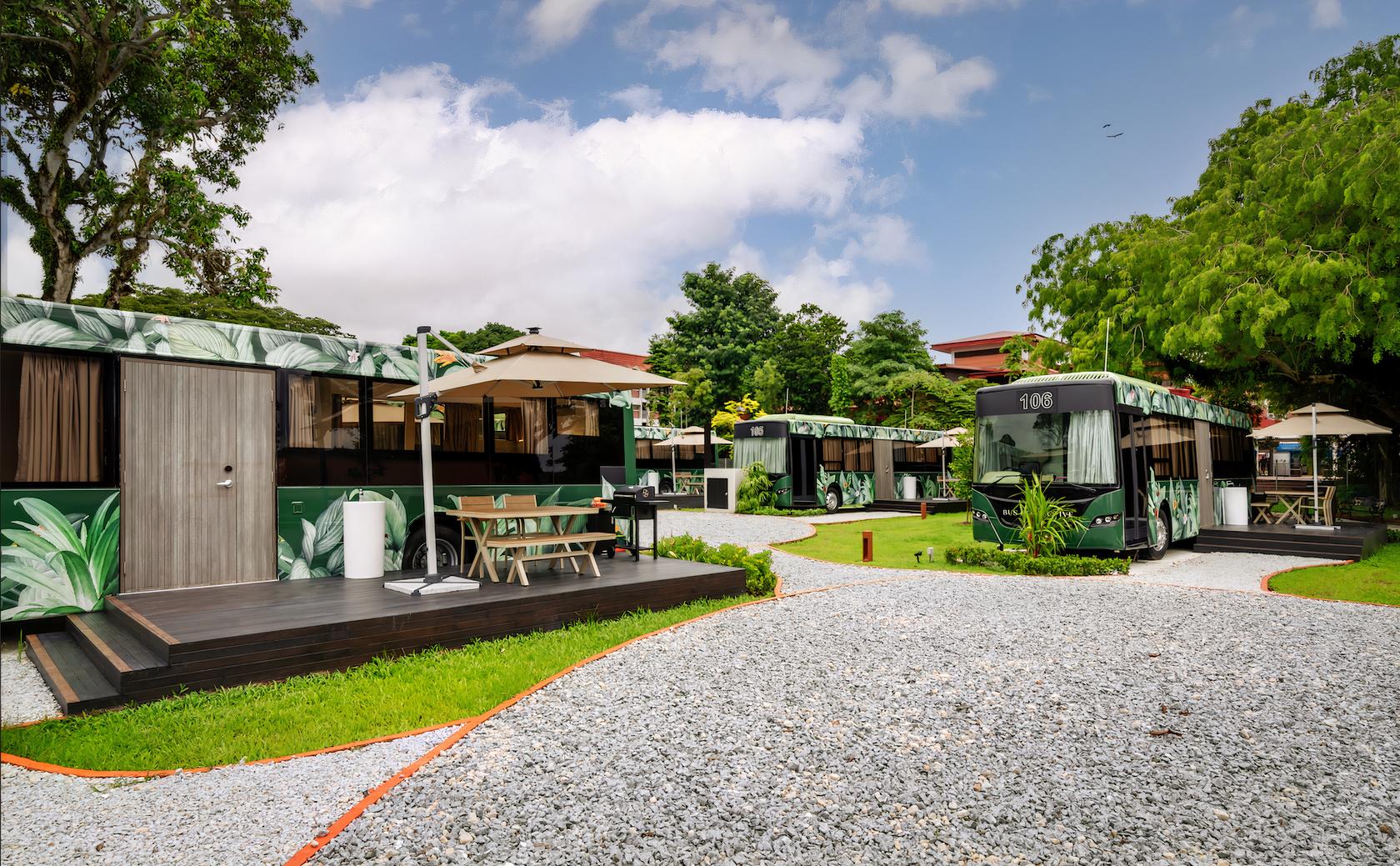 A row of converted party buses with outdoor seating areas, large windows, and umbrellas at The Bus Collective.
