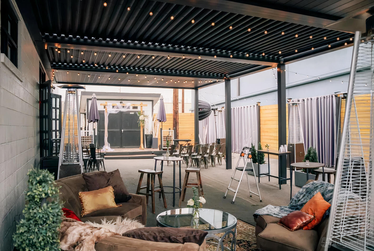 An event venue with a covered patio, string lights, lounge seating, and tall tables at Evolve at Mile Hi.
