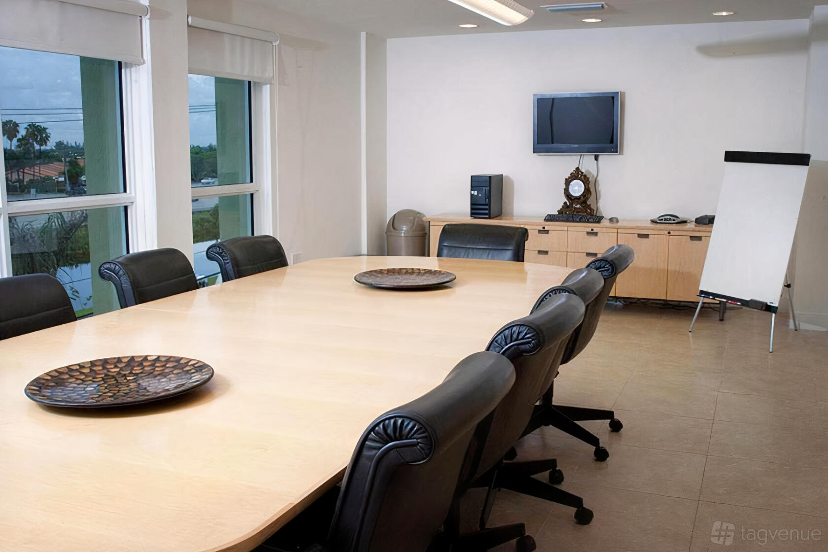An auditorium conference room with a long wood table, black leather chairs, windows, and a flip chart at South River Suites.