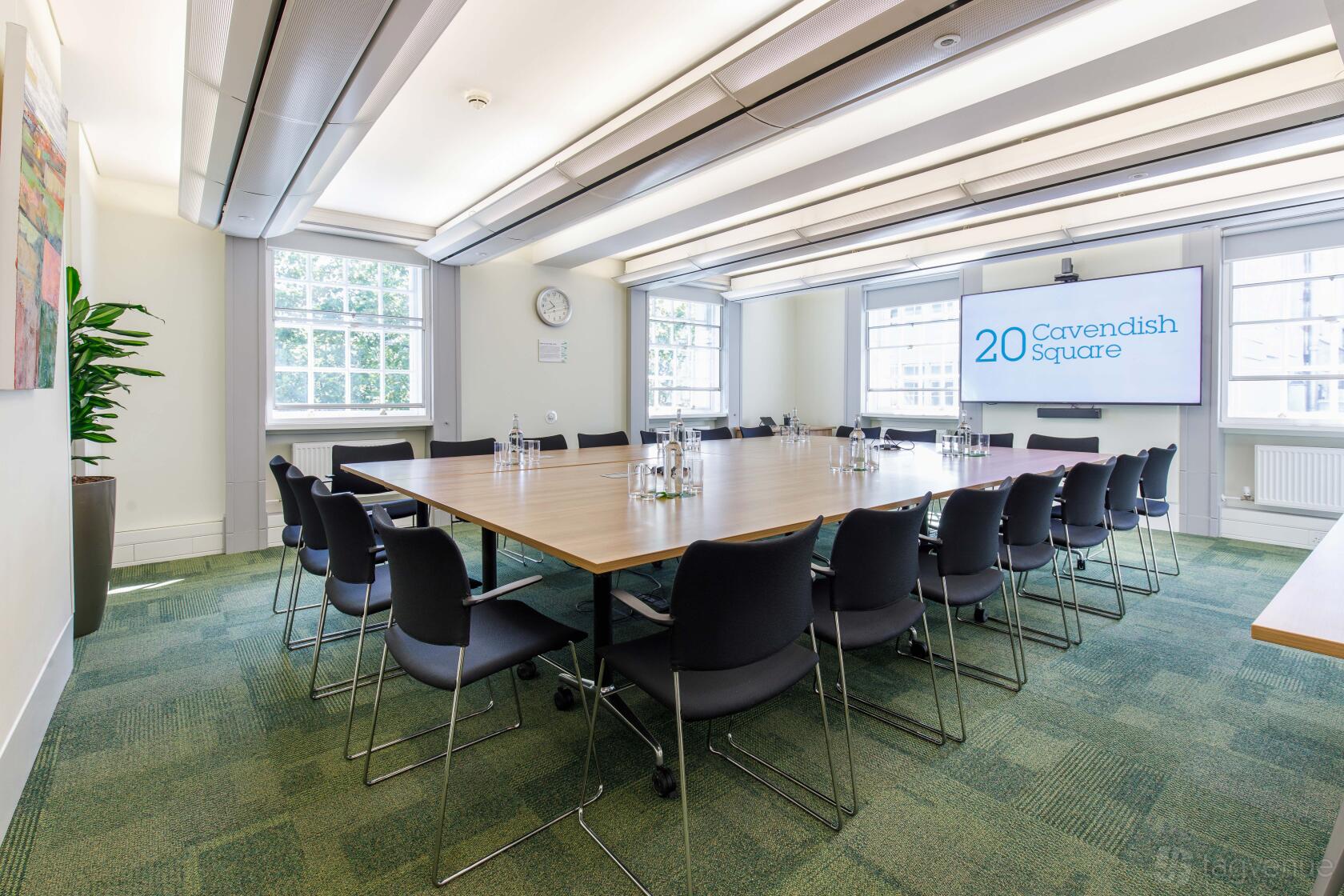 A meeting room with a U-shaped table setup, black chairs, and large windows at 20 Cavendish Square.