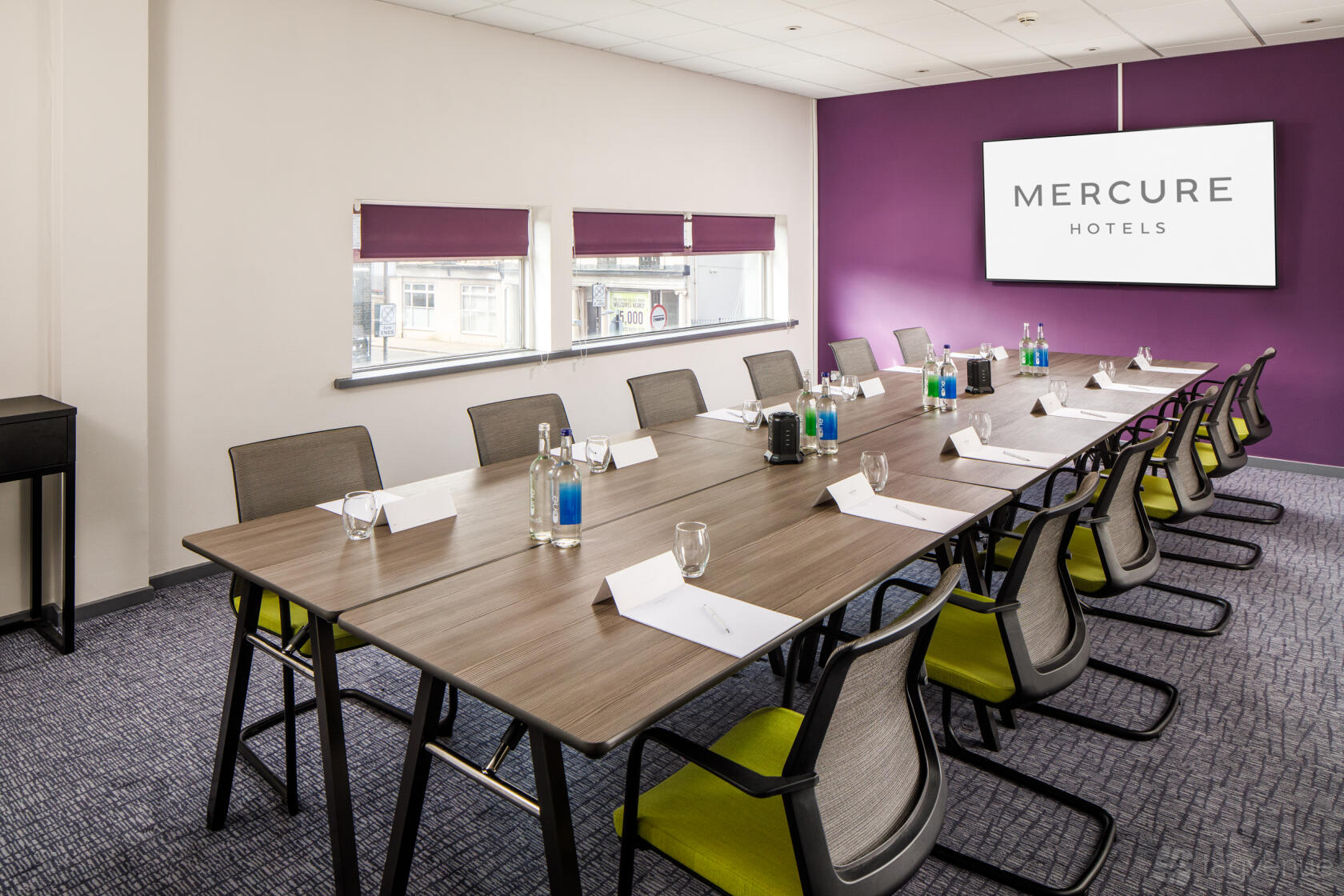 A meeting room with a long conference table, ergonomic chairs, and a wall-mounted screen at Mercure Bedford Centre.