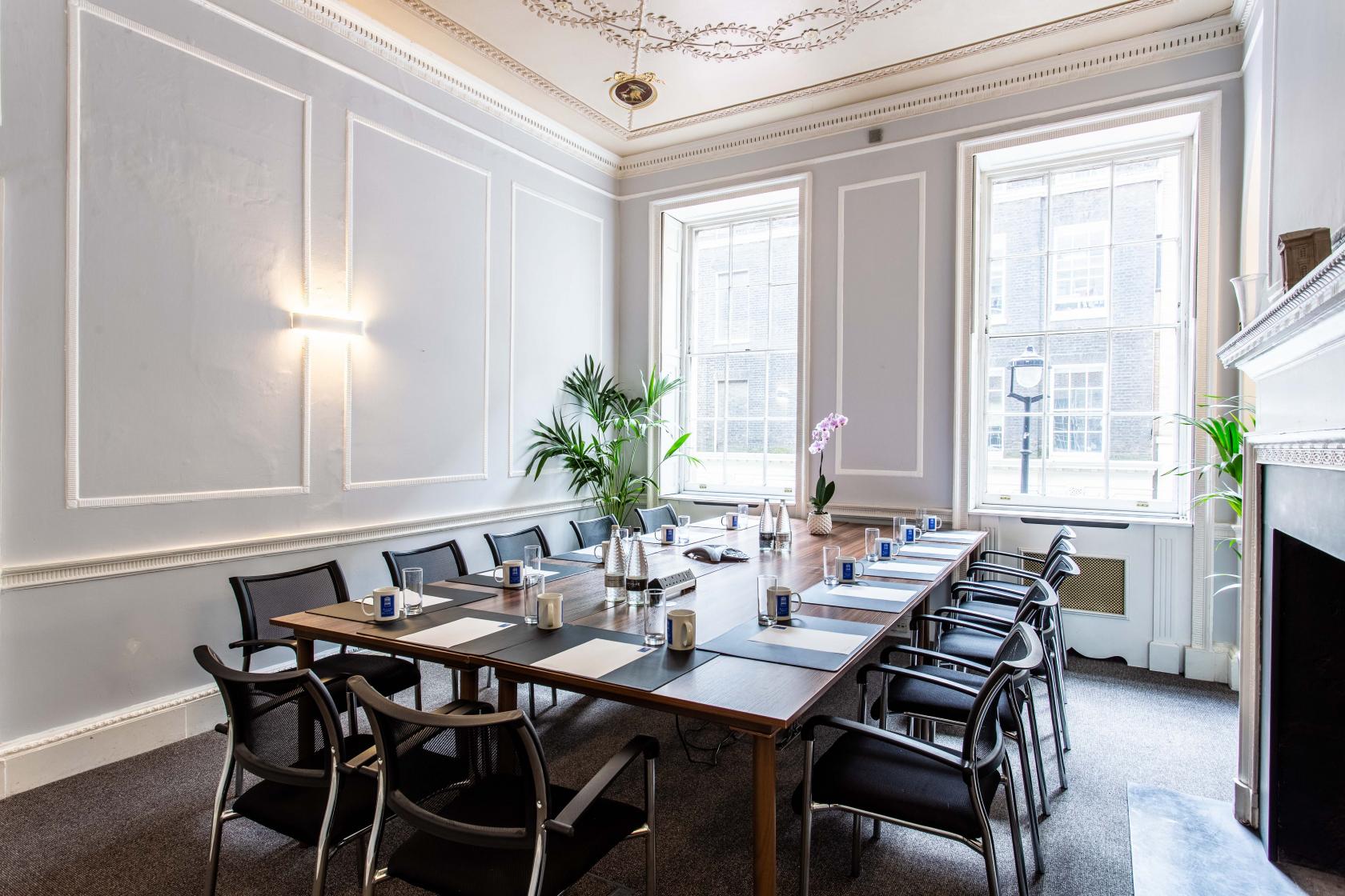 An event venue with a long conference table, black chairs, tall windows, and decorative molding at Adam House Event Space.
