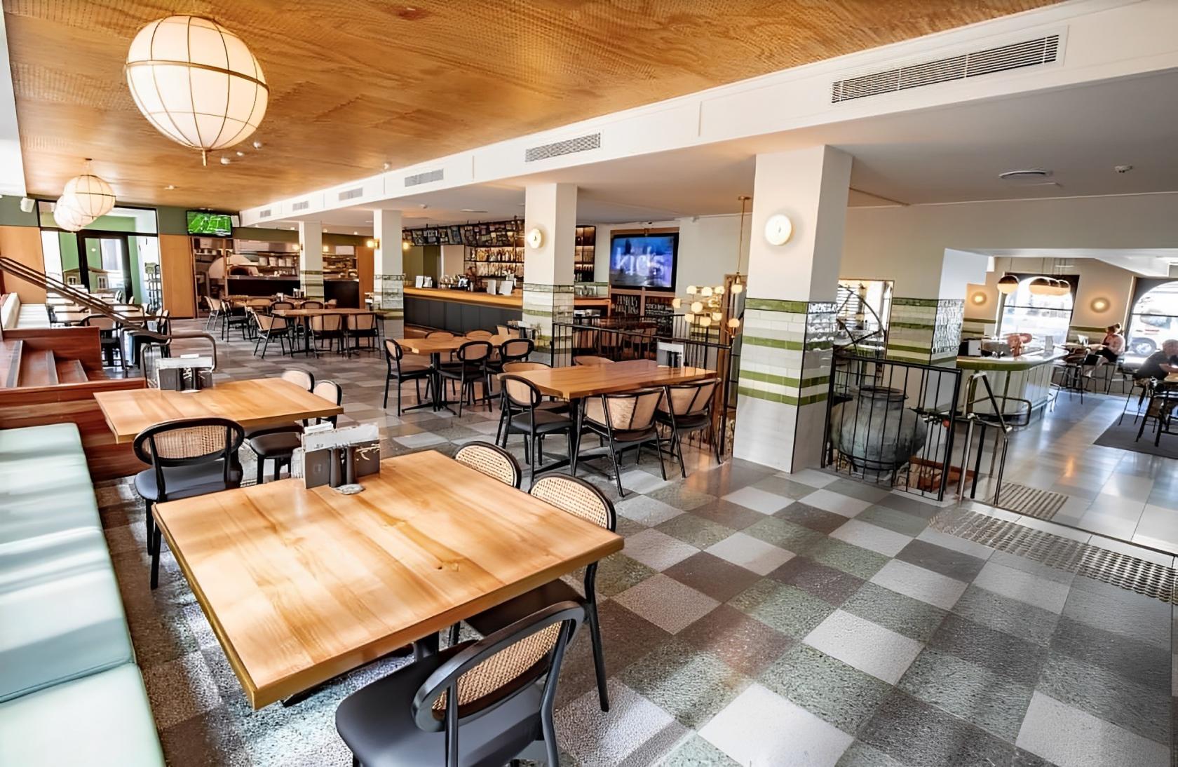 A hotel restaurant with wood tables, checkered tile floors, and a central bar at Southern Cross Hotel.
