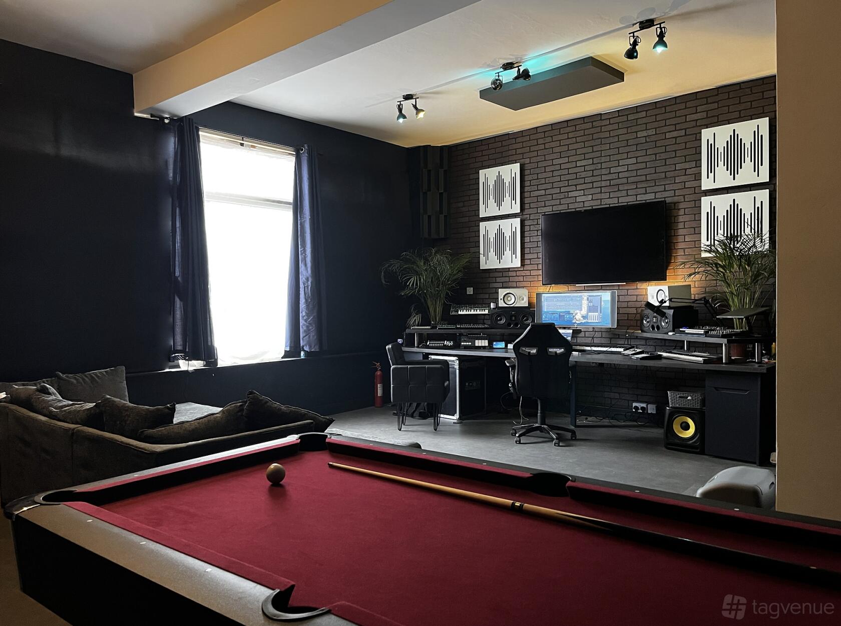 A recording studio with soundproofed walls, audio equipment, a red pool table, and lounge seating at Fusion Creative Studios.