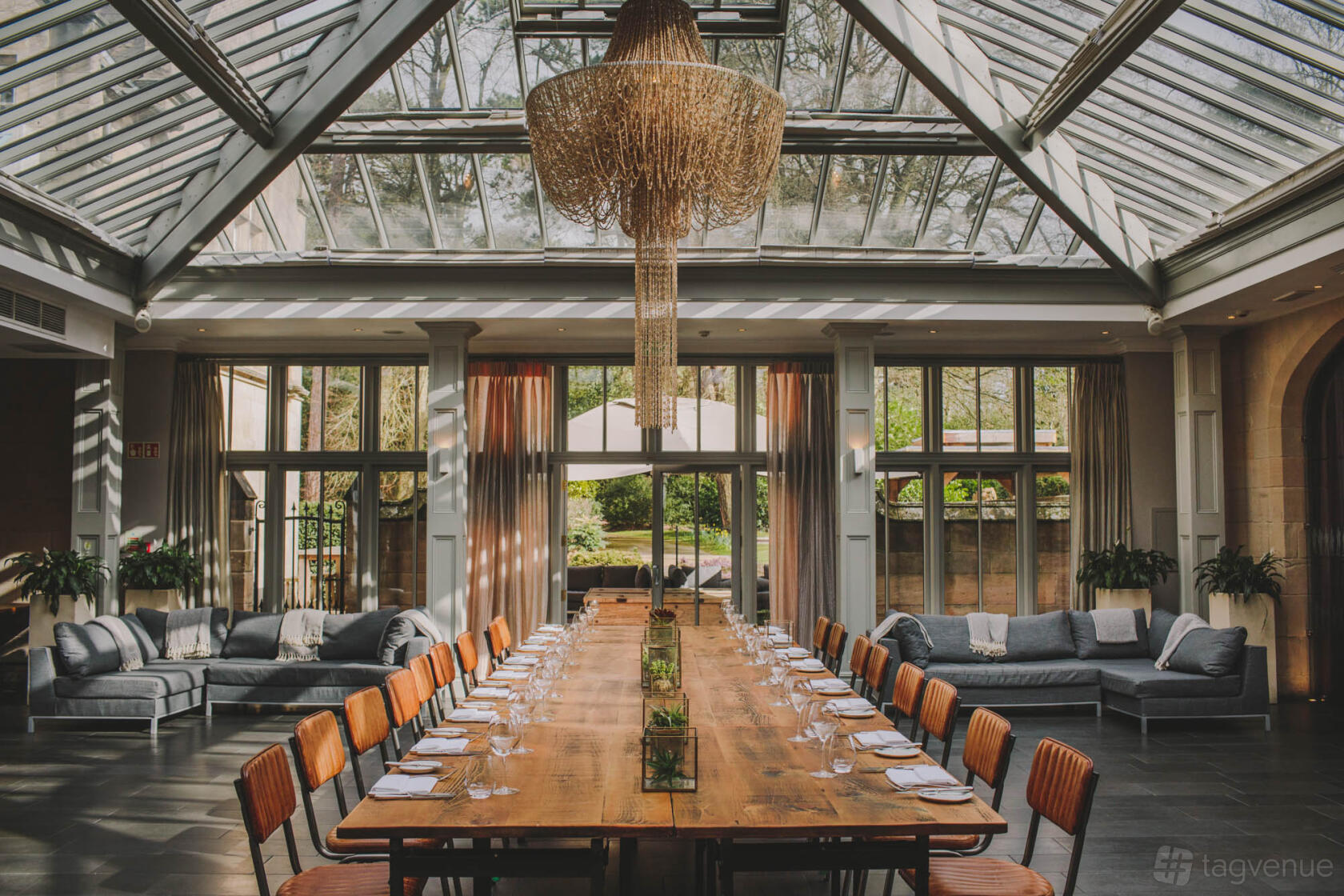 An event space with a glass ceiling, chandelier, long wooden table, and sofas at Hampton Manor.