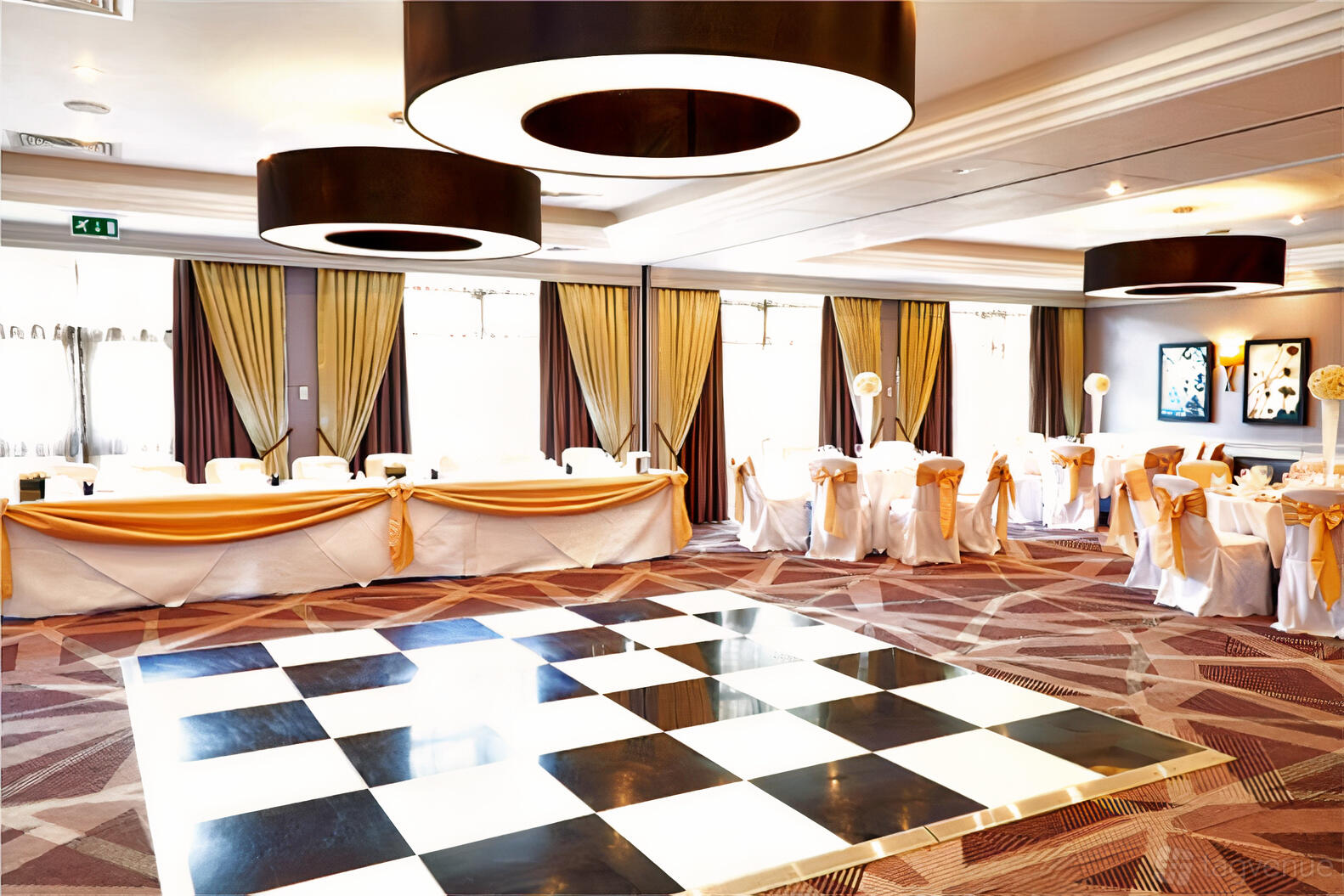 A hotel hall with large windows, checkered dance floor, draped curtains, and banquet chairs at DoubleTree by Hilton London - Ealing.