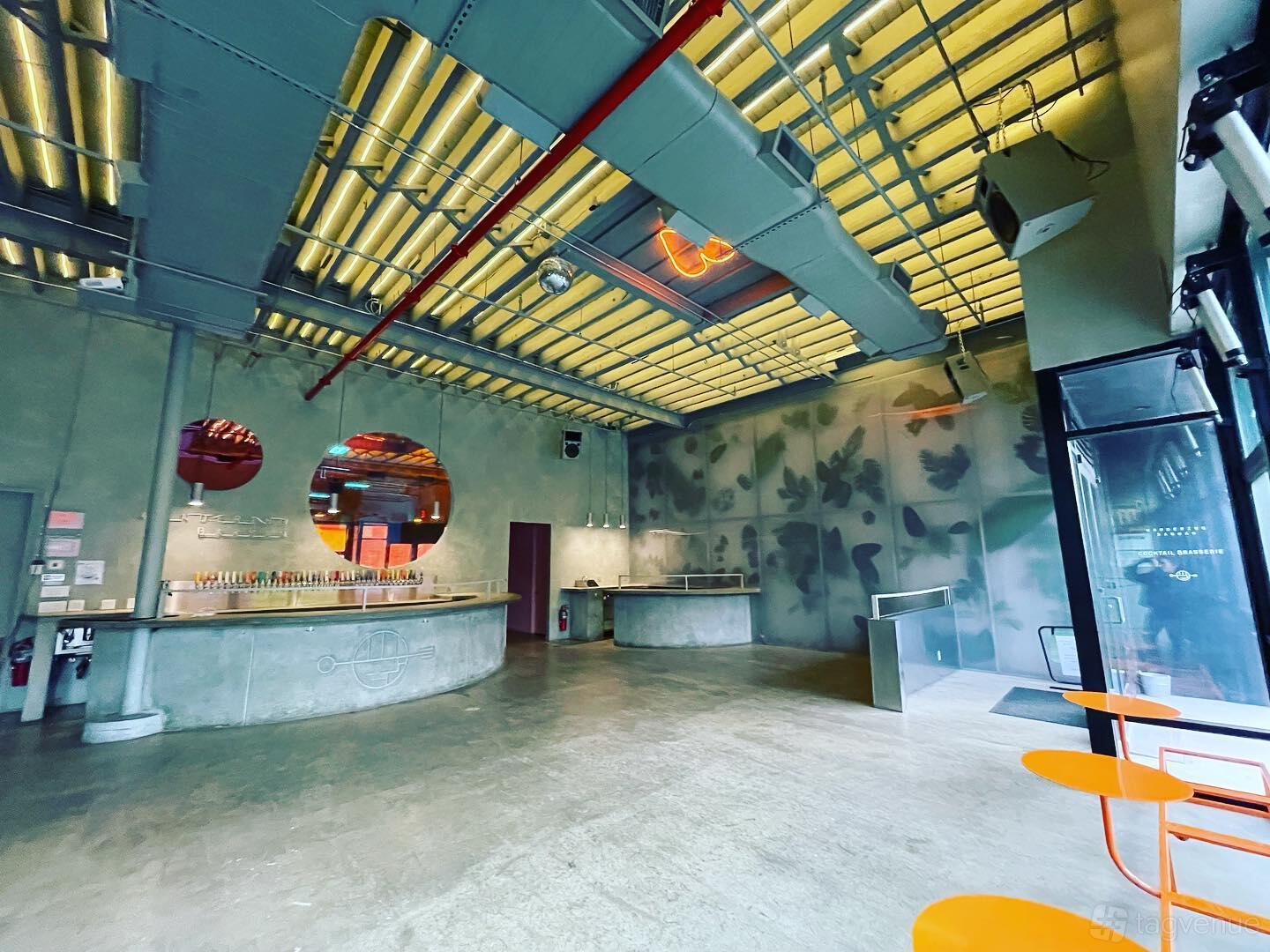 An event space in a bar with polished concrete floors, exposed ceiling beams, and a curved bar at Wandering Barman.