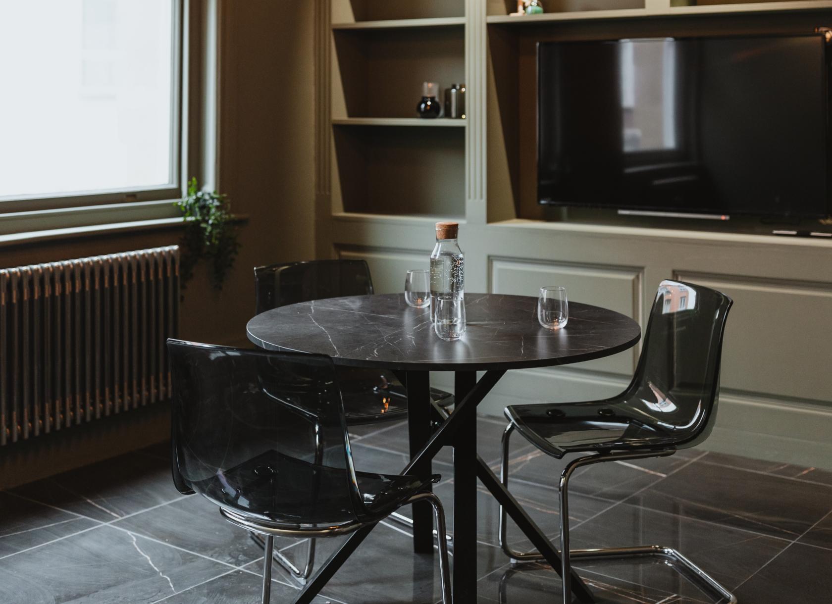 A meeting room with a round black table, transparent chairs, built-in shelves, and a wall-mounted TV at Armada House.