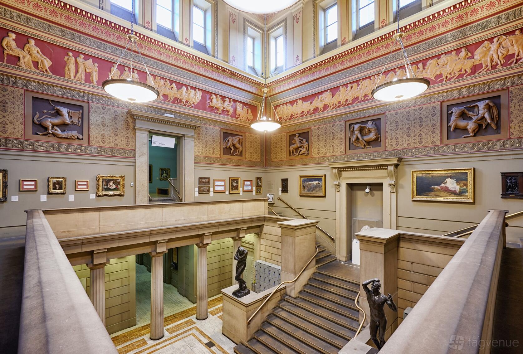 A grand hall with ornate classical murals, framed paintings, and statues at Manchester Art Gallery Victorian Hall.