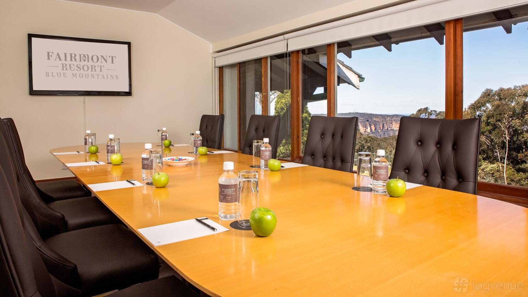 A meeting room with a large wooden table, leather chairs, notepads, and windows overlooking mountain views at Fairmont Resort Blue Mountains.