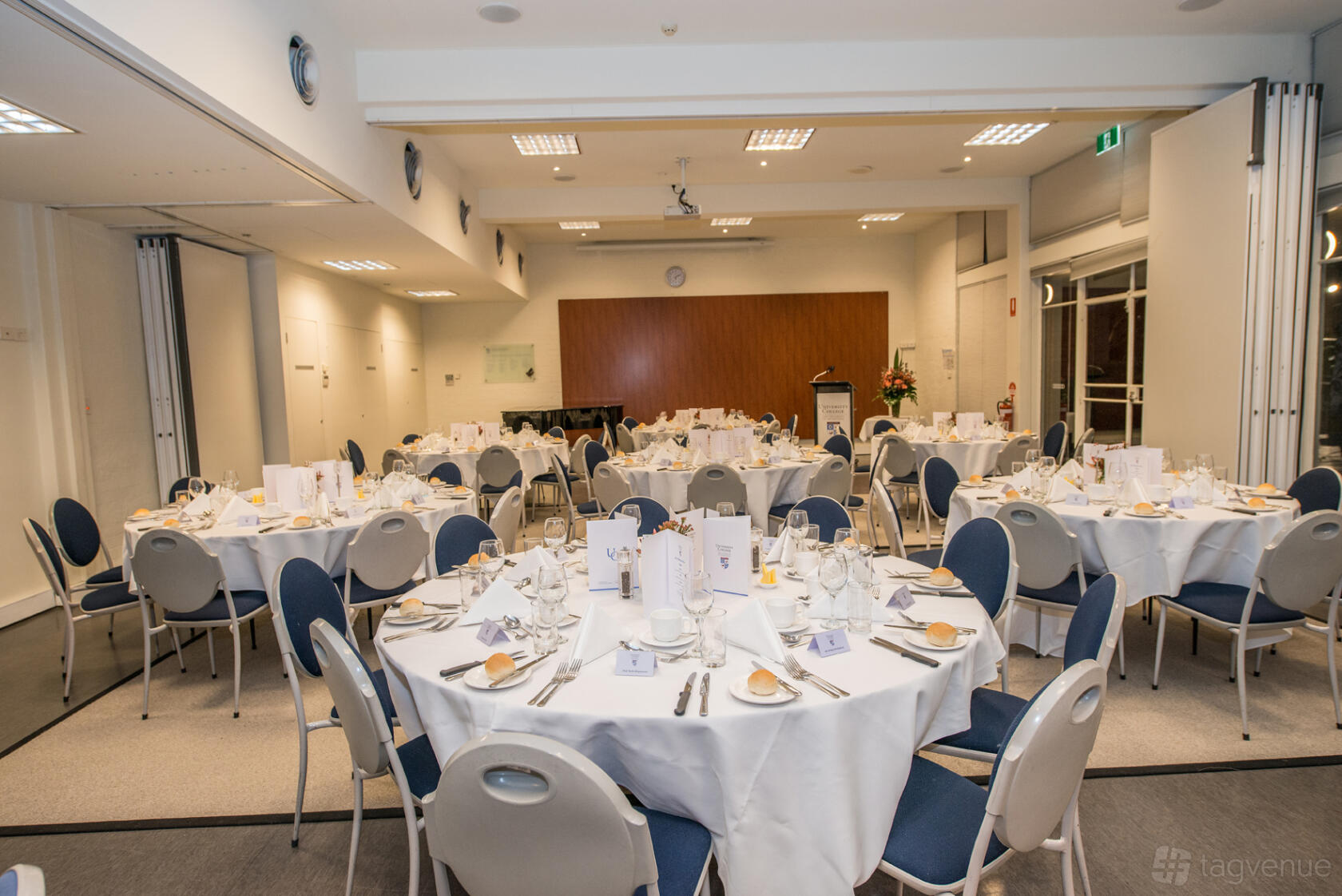 An event space with round tables set for dining, navy chairs, and wood paneling at University College.