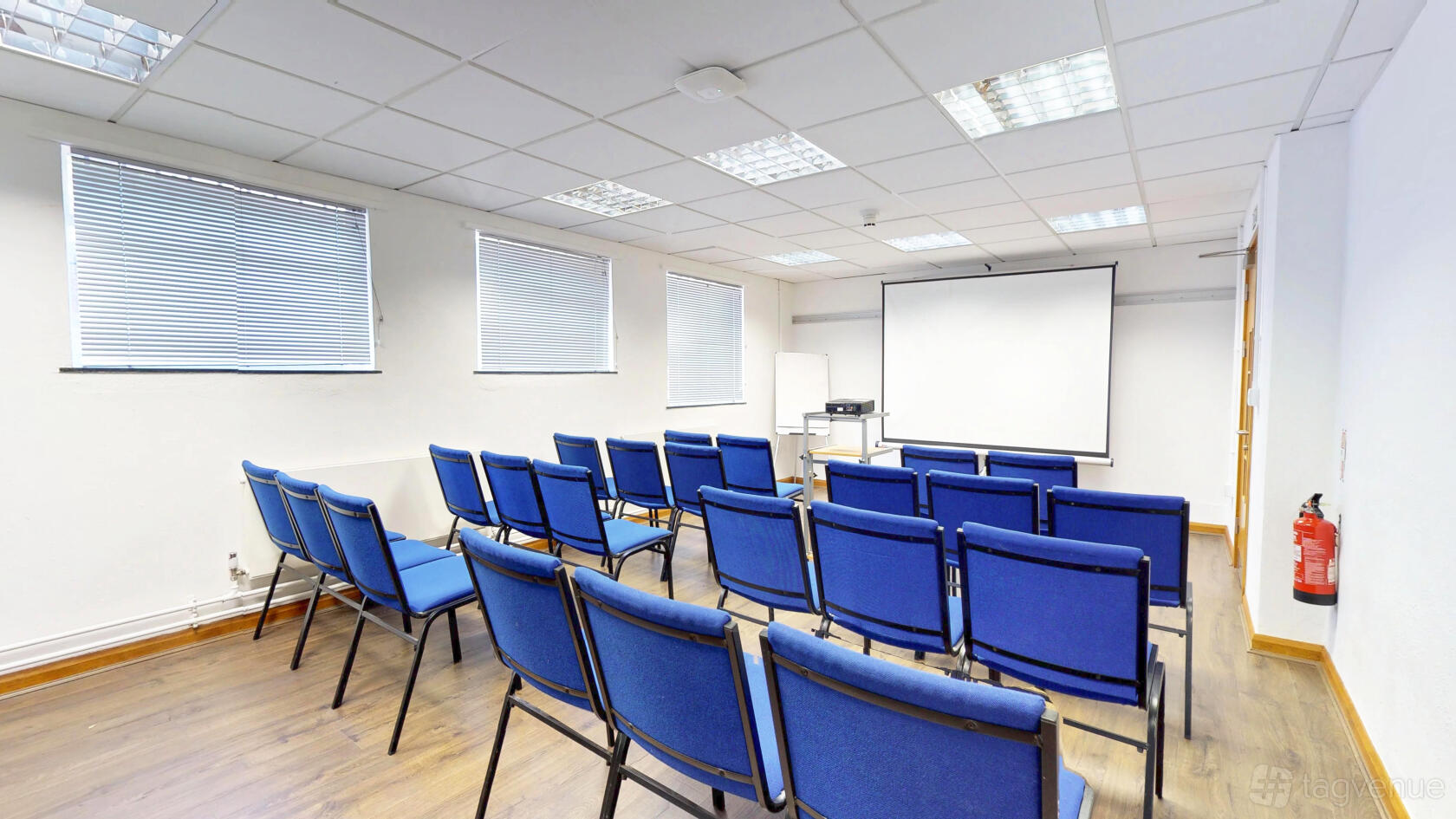 A meeting room with rows of blue chairs, wood flooring, and a projector screen at The Upper Norwood Library Hub.