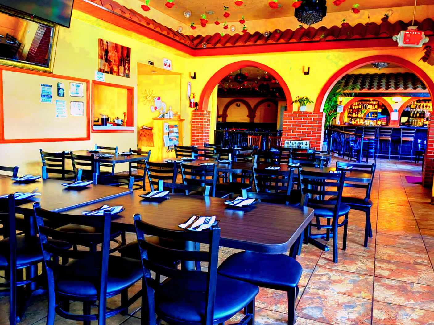 A restaurant with tiled floors, wooden tables set with napkins, and arched brick accents at Il Saggio Italian Restaurant.