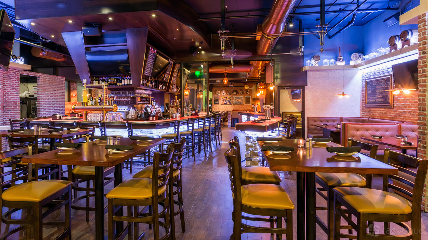 A restaurant with wood tables, high-top chairs, an illuminated bar, and exposed ductwork at Batch Gastropub - Miami.