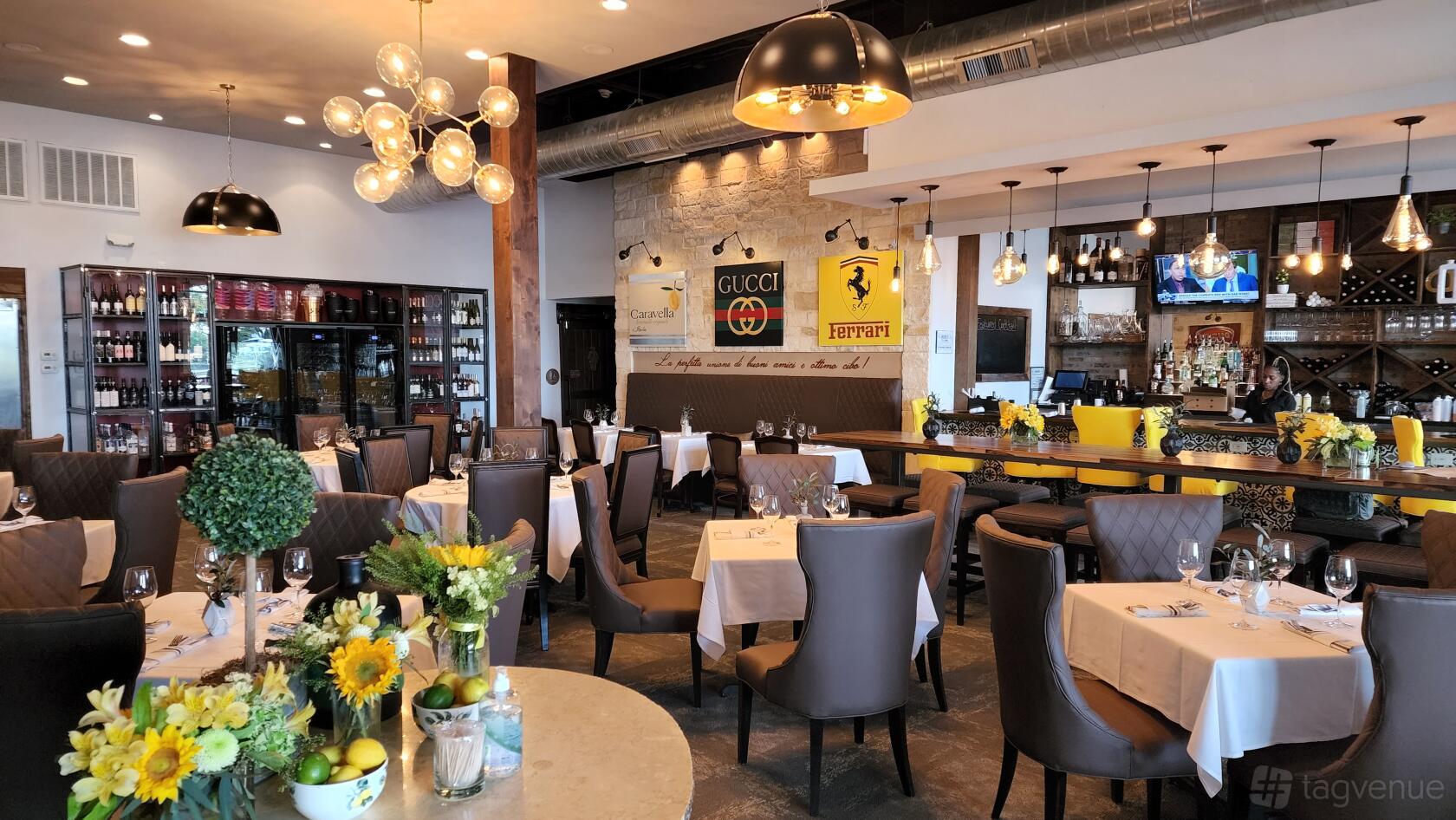 A restaurant with white tablecloths, fresh floral centerpieces, leather chairs, and exposed ductwork at Passerella.