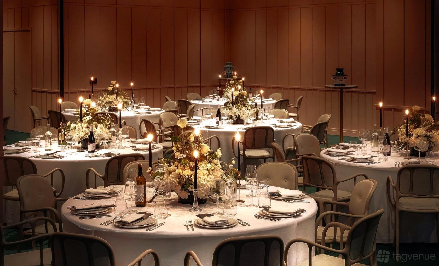An event space with round tables dressed in white linens, floral centerpieces, and candlelight at art'otel London Battersea Power Station