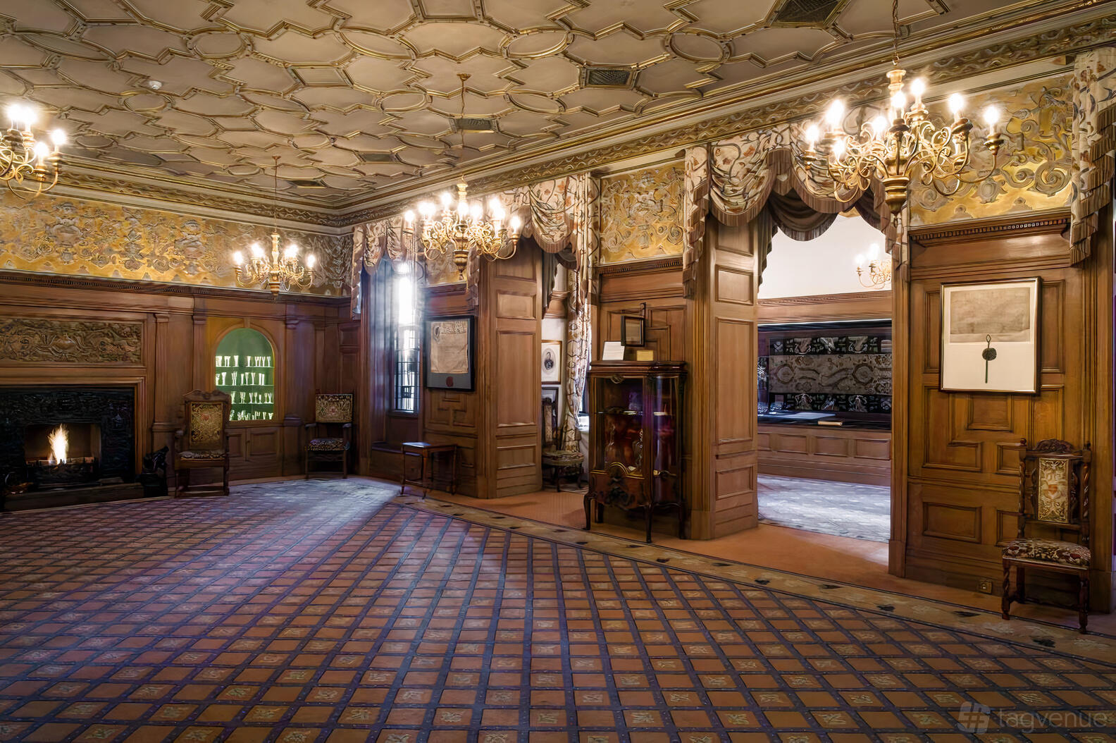An event space with wood paneling, ornate chandeliers, patterned ceiling, and a fireplace at Vintners' Hall.