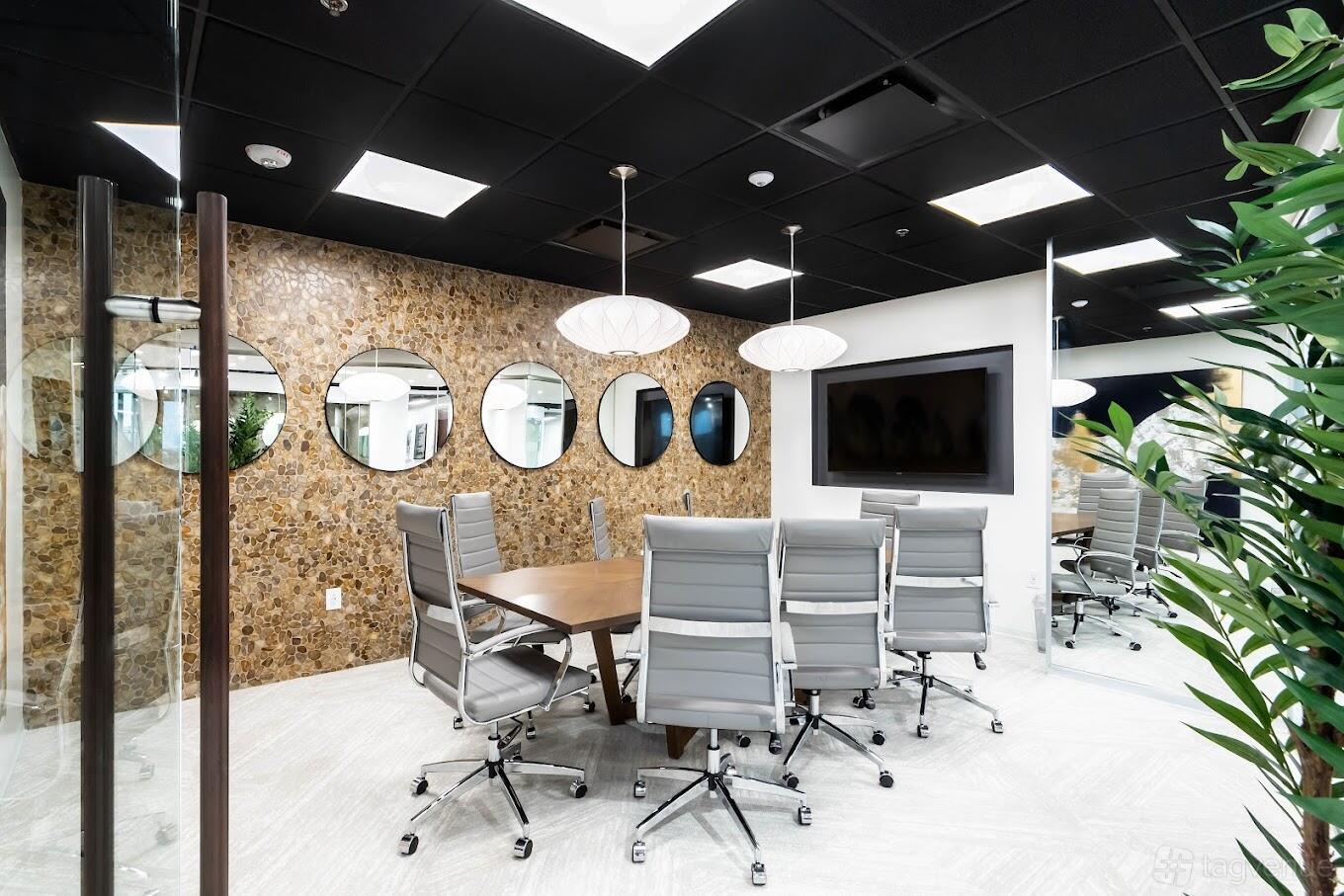 A boardroom with a wood accent wall, circular mirrors, pendant lighting, and gray chairs at Lucid Private Offices - Alpharetta Atlanta.