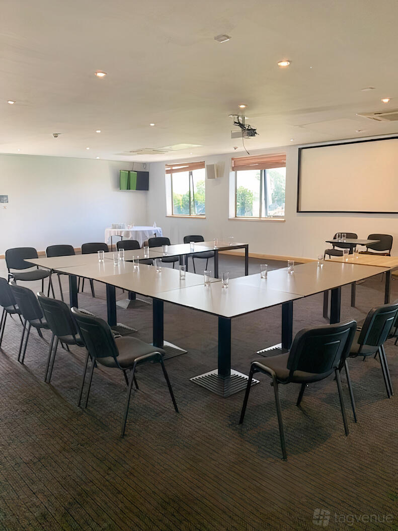 A conference room with a U-shaped table setup, black chairs, and large windows at The Thames Club Health Club.