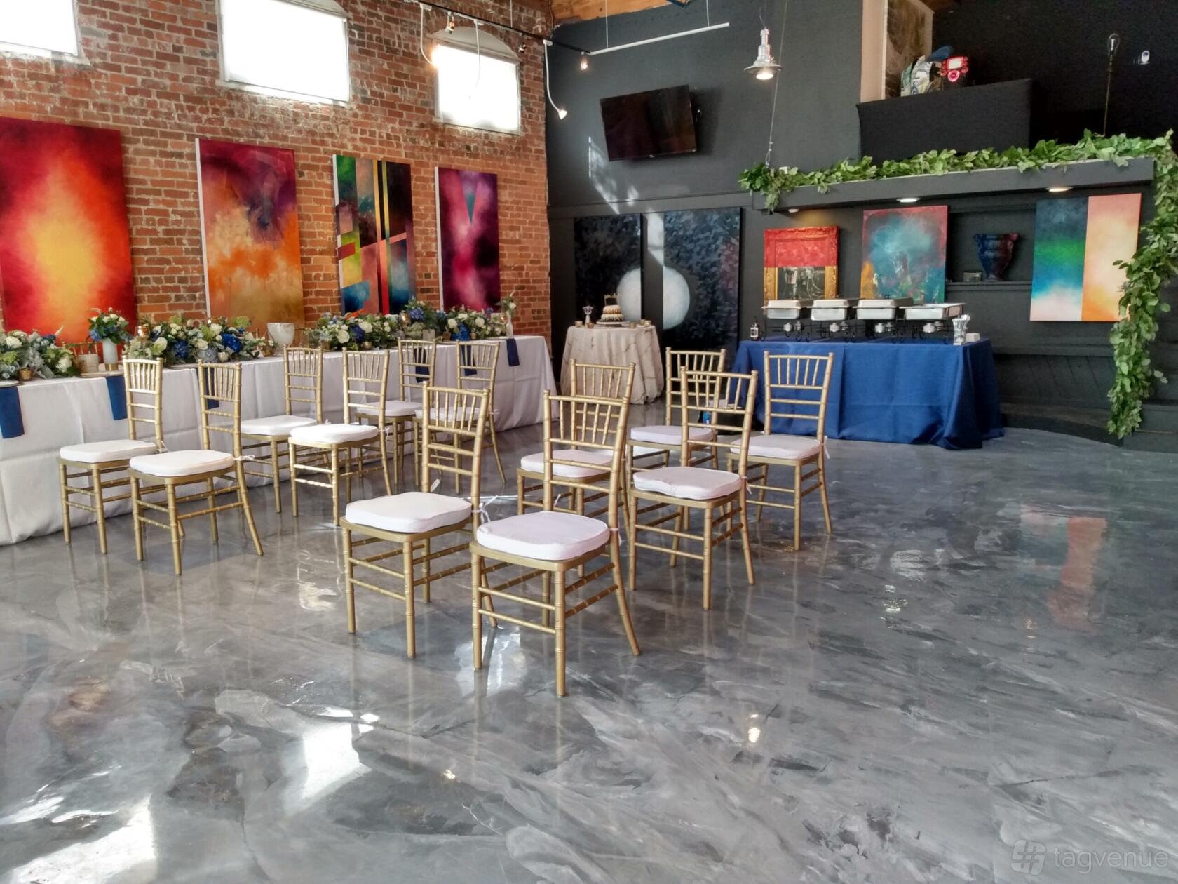 A gallery with abstract paintings on exposed brick walls, polished floors, and gold chairs at Bisong Art Gallery.