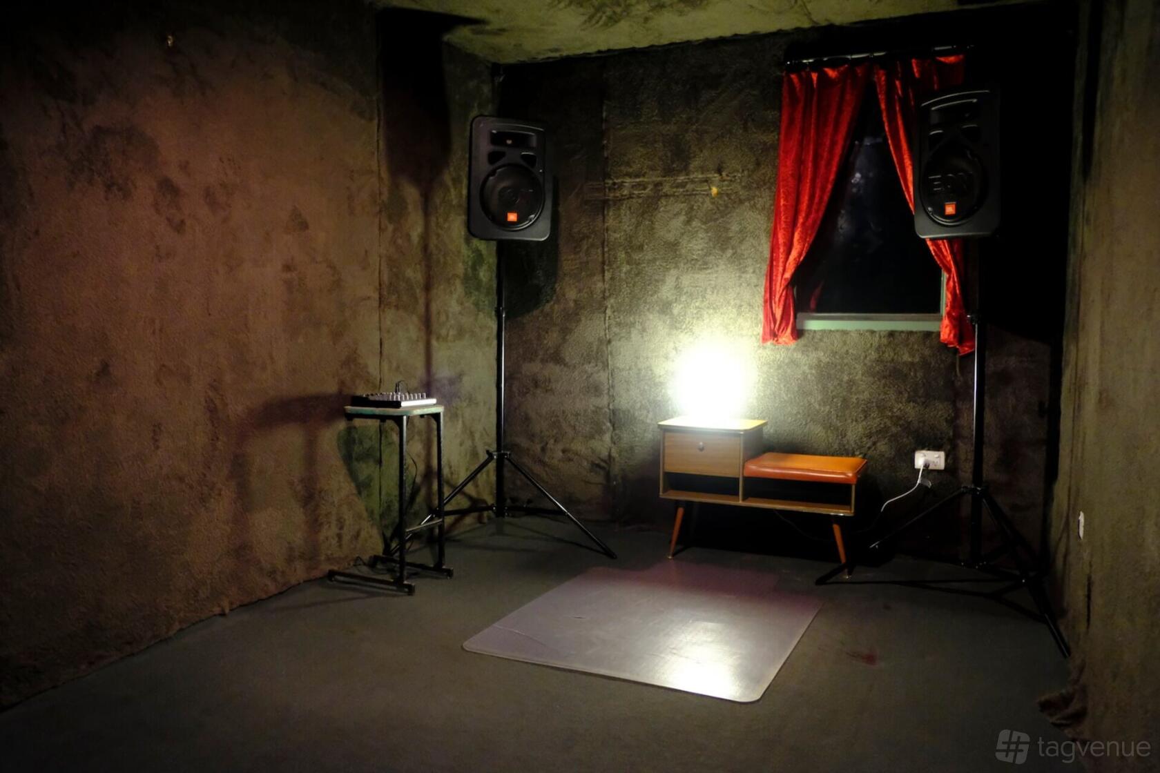A recording studio with soundproofed dark walls, two large speakers, red curtains, and a mixing console at Cactus Room.