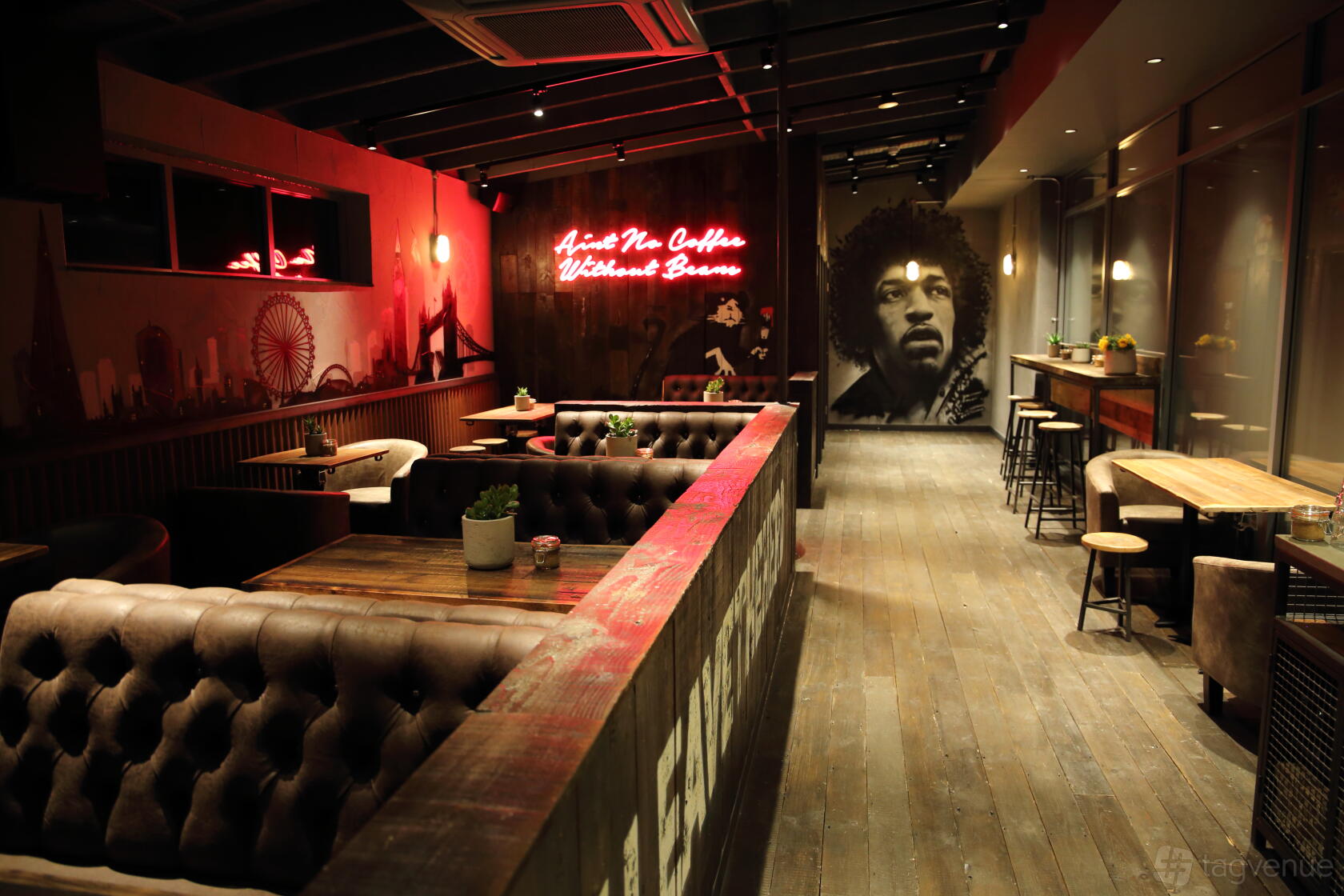 A cafe with tufted leather booths, wooden floors, neon signage, and a mural at Black Sheep Coffee Wembley.