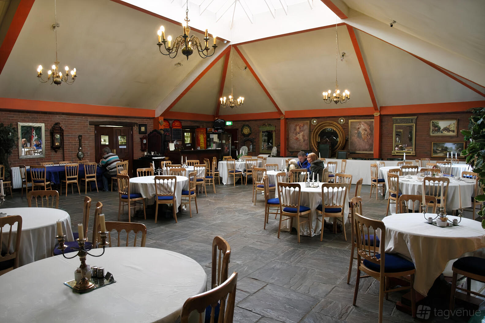 A hall with round tables covered in white linens, chandeliers, and skylight ceiling at Heskin Hall.