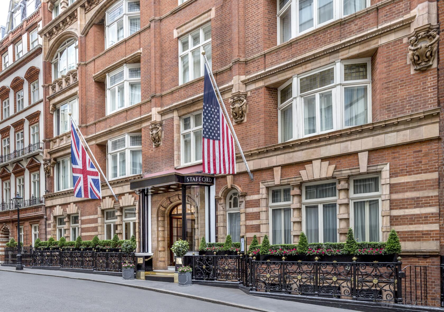 A hotel entrance with large arched doorway, brick facade, and flag displays at The Stafford London.