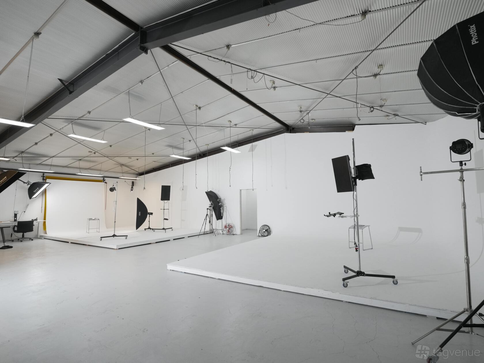 A bright photo studio with a large white cyclorama, overhead lighting, and professional photography equipment at Valeon Studio.