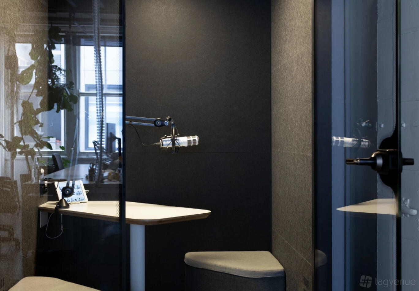 A small meeting room with a glass door, built-in microphone, and corner desk at Desk Space.