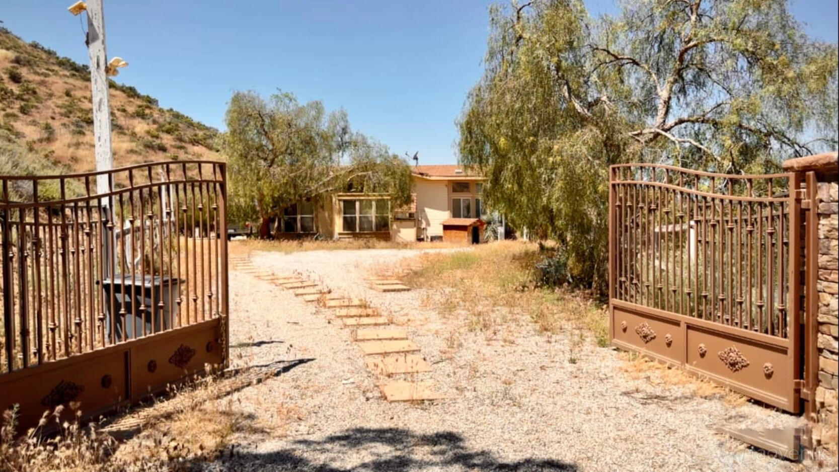 A country house with a gravel driveway, open iron gates, and surrounding trees at Sierra Outpost.