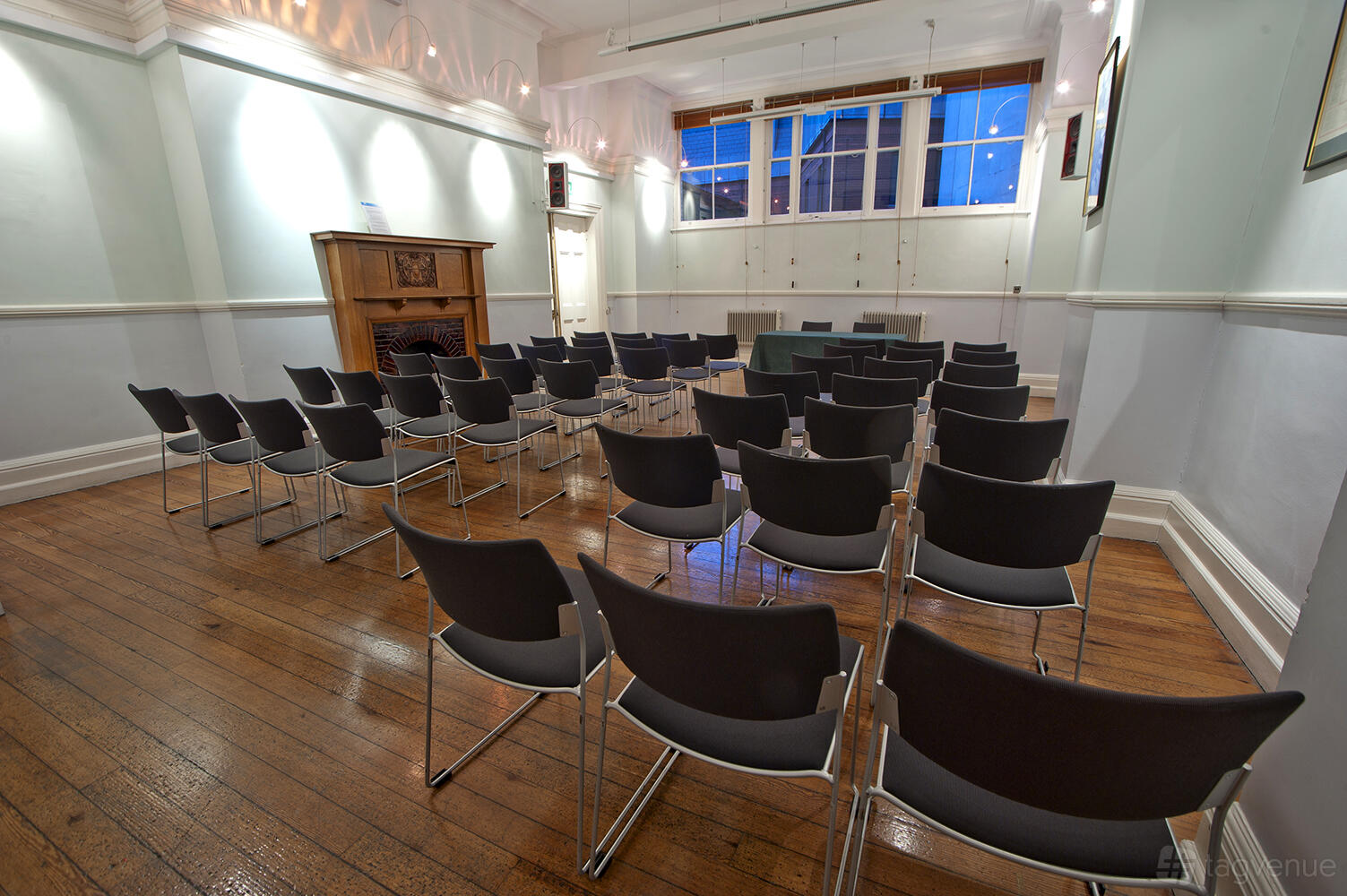 An event space with rows of black chairs, wooden floors, and a decorative fireplace at St Bride Foundation.