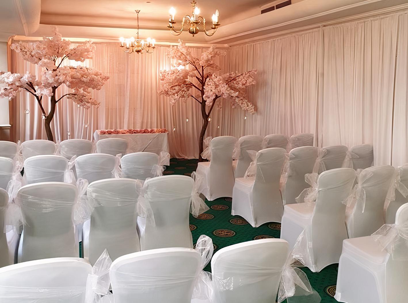 An event space with rows of white chair covers, green carpeting, and pink blossom trees at Atlantic Tower Hotel Liverpool By Sunday.